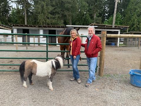 Two people and pony on one side of a gate and another horse on the other side in front of Washington stables.