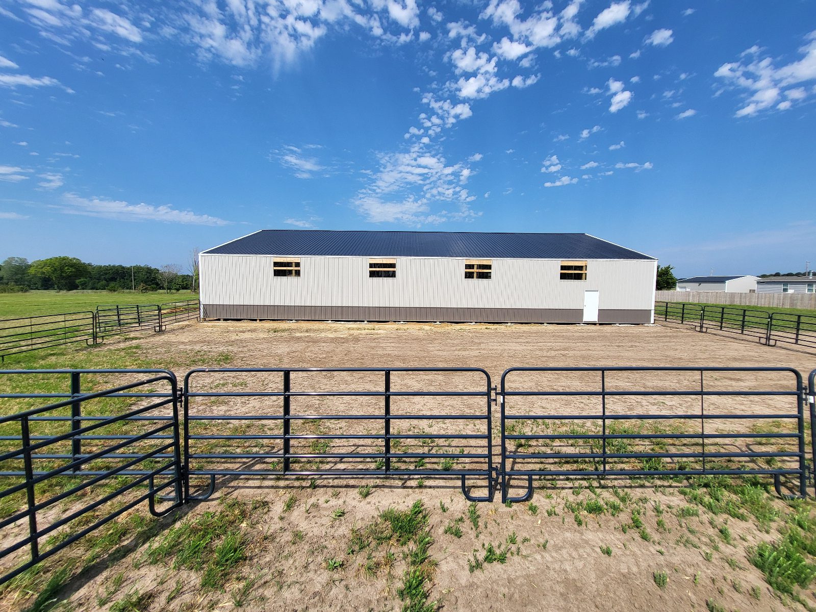 An image of an enclosed arena in Oklahoma from the outside with blue skies and a few fenced outdoor areas.